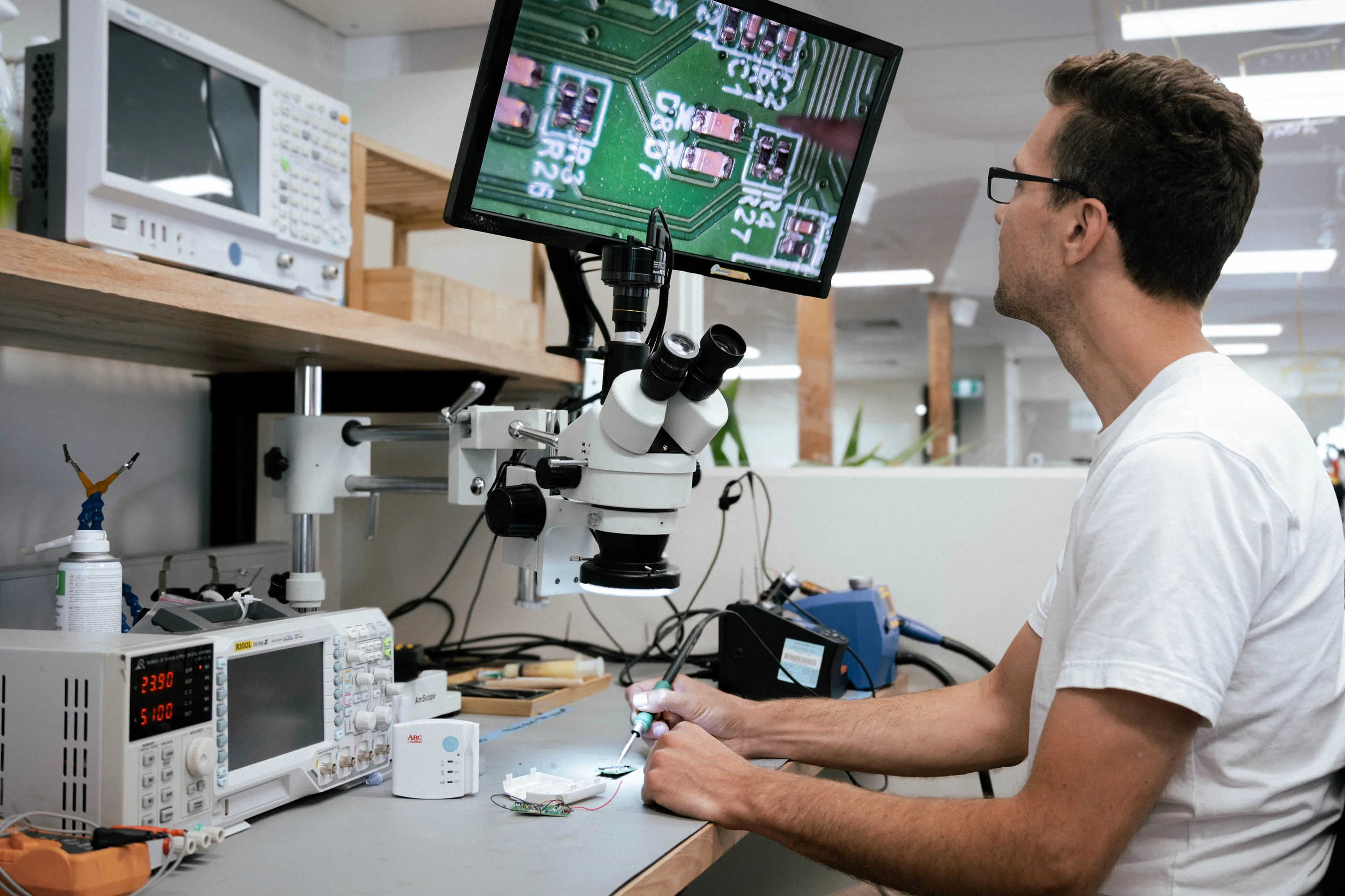 PCB inspection and testing under a microscope. Engineer holding a soldering iron
